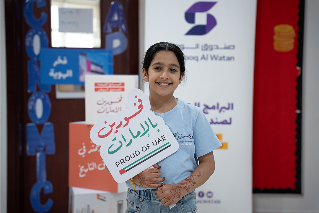 Child holding a Sandooq Al Watan banner during an event